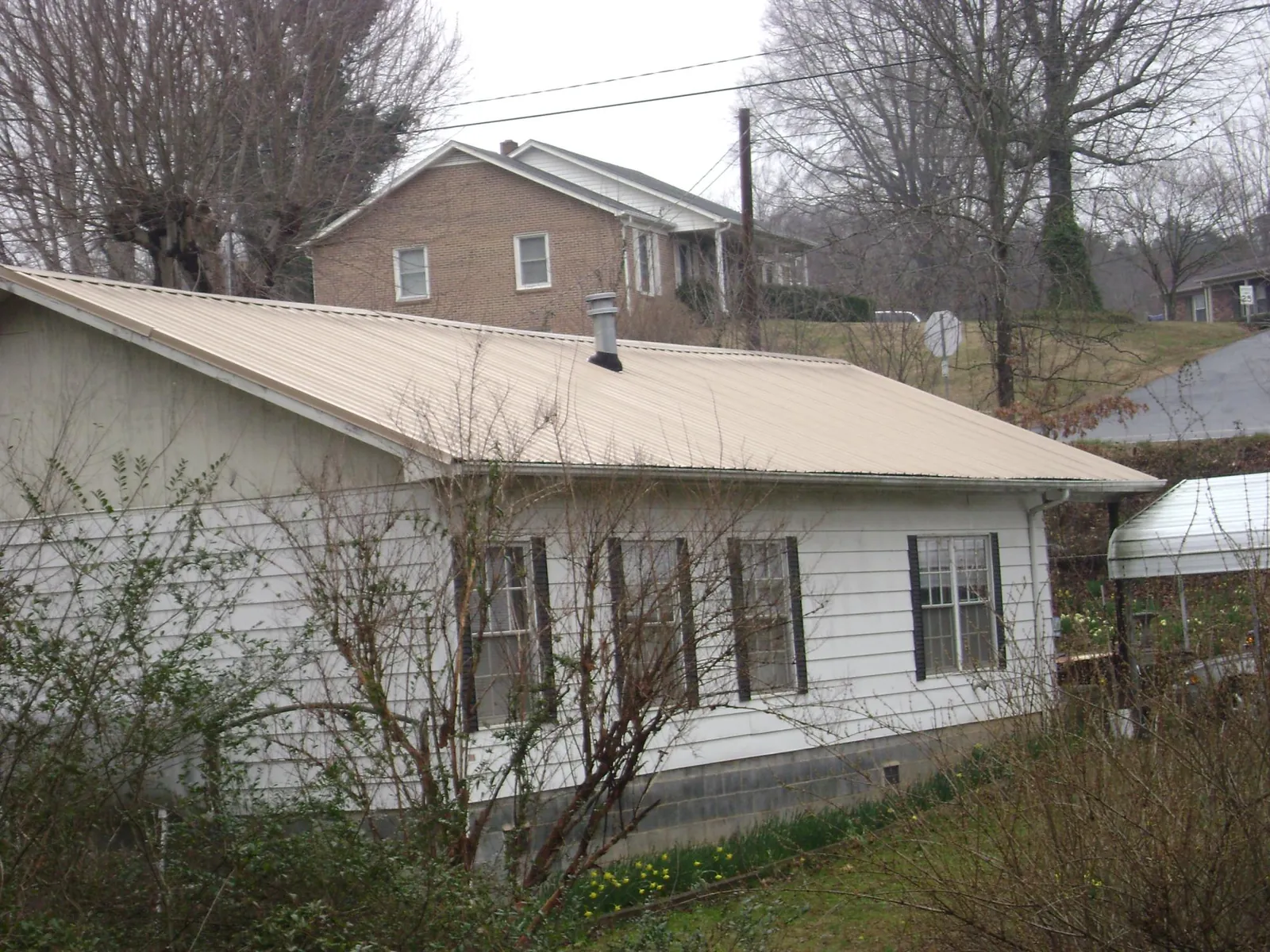 Tan metal roof on a white sided house set into a hillside — Commercial Roofing by Roofing Brothers in Pacific